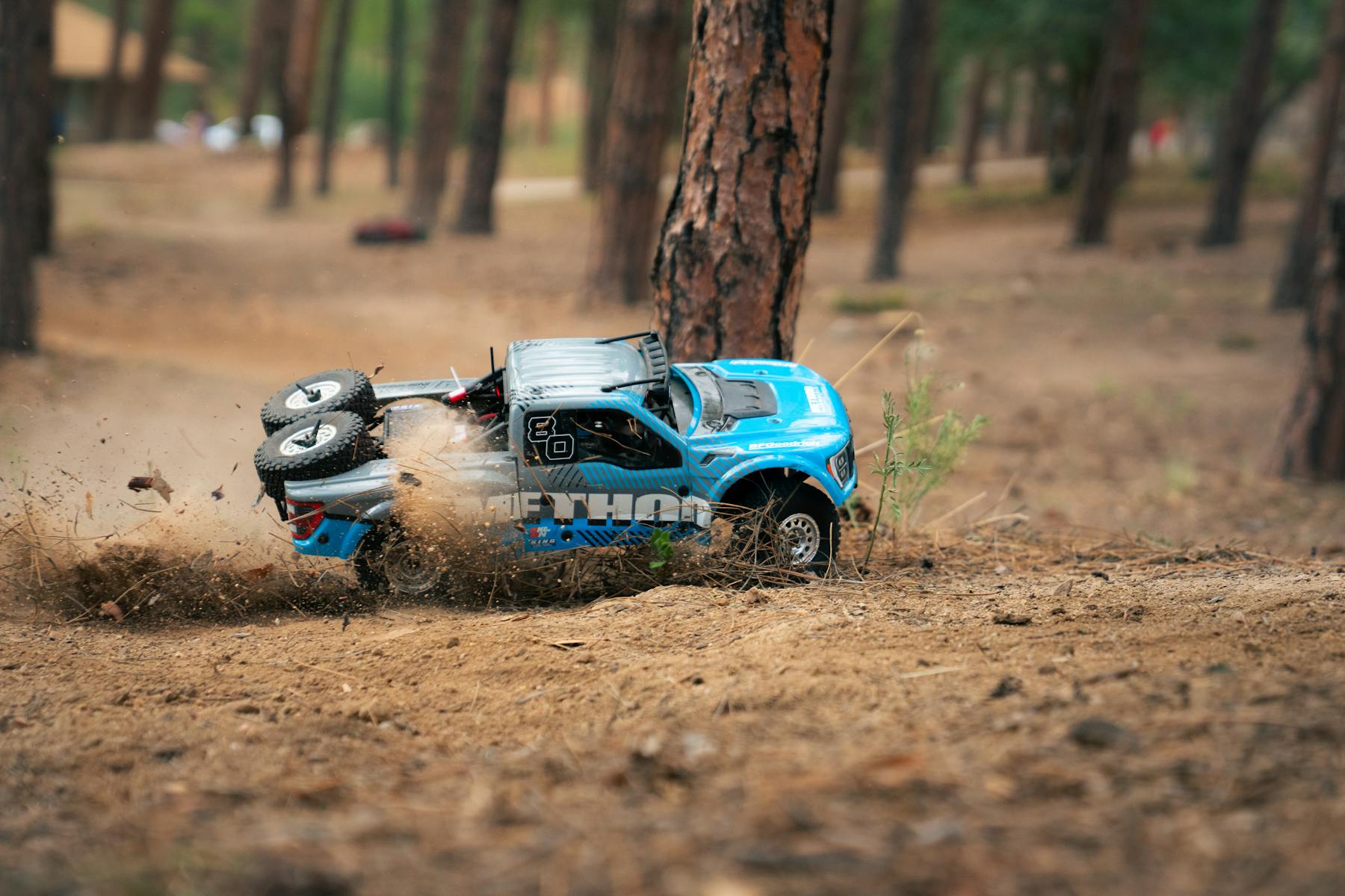 Blue RC truck sliding through dirt beside a tree