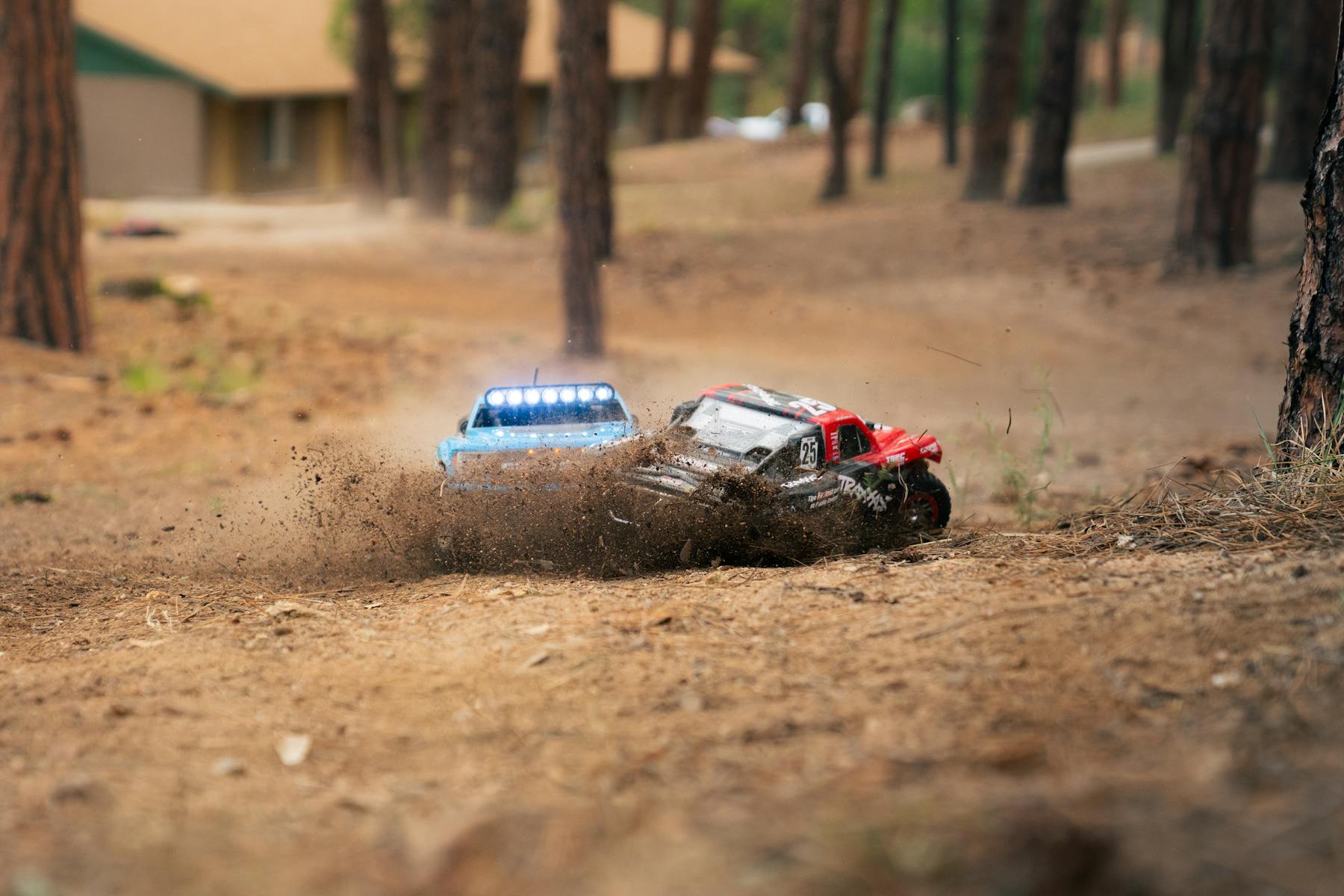 Two RC cars kicking up dirt while racing through a forest track